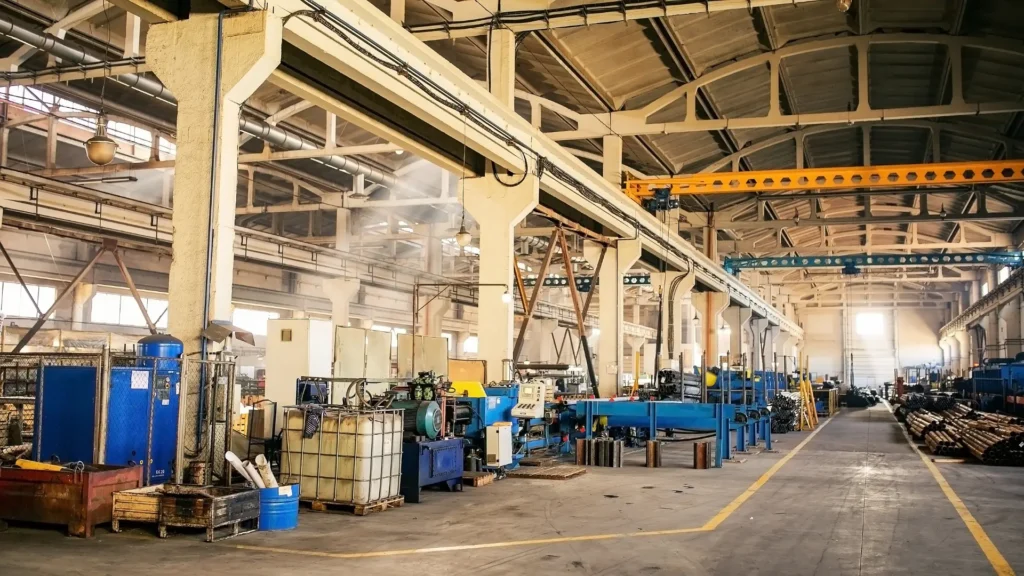 Large industrial factory interior with high ceilings, machinery, storage containers, and metal