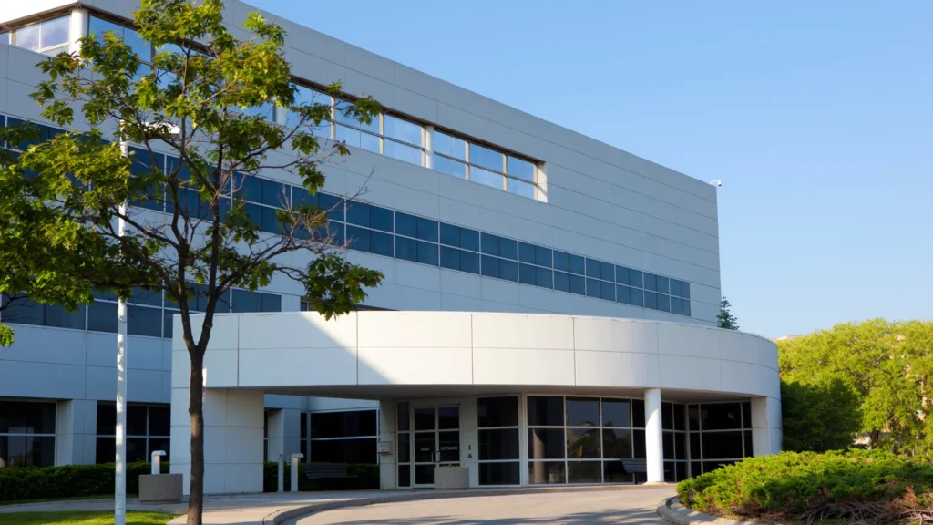 A modern office building with large windows and a curved entrance, surrounded by trees and