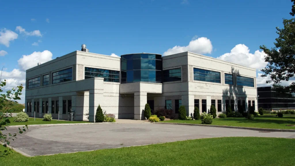 A modern two-story office building with large windows, white exterior walls, and landscaped