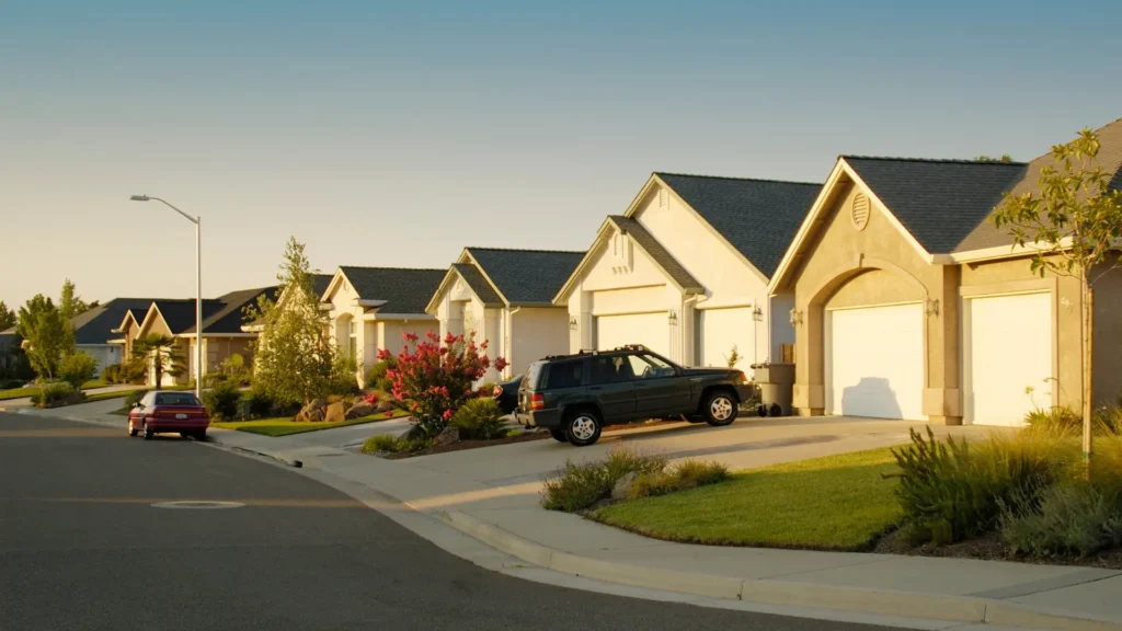 A row of modern suburban houses with garages and driveways on a quiet street, with two parked cars