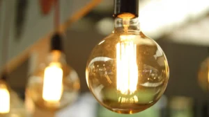 A close-up of a glowing round light bulb with visible filaments, with similar bulbs blurred in the