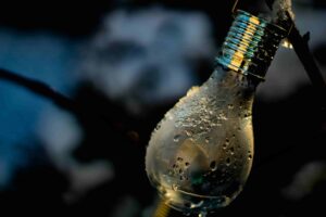 A close-up of a light bulb covered in water droplets and frost, hanging outdoors with a dark