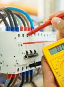 A person uses a digital multimeter to test electrical connections on a circuit breaker panel with