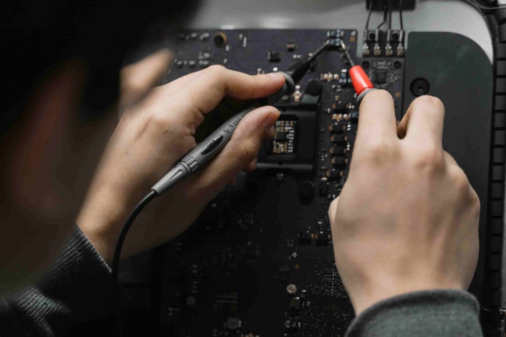 Close-up of hands using test probes to examine components on a circuit board—a perfect example when considering What Questions to Ask Before Hiring Electricians?.